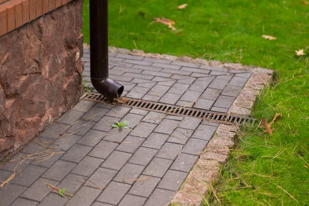Downspout directing water into a drain away from hardscape